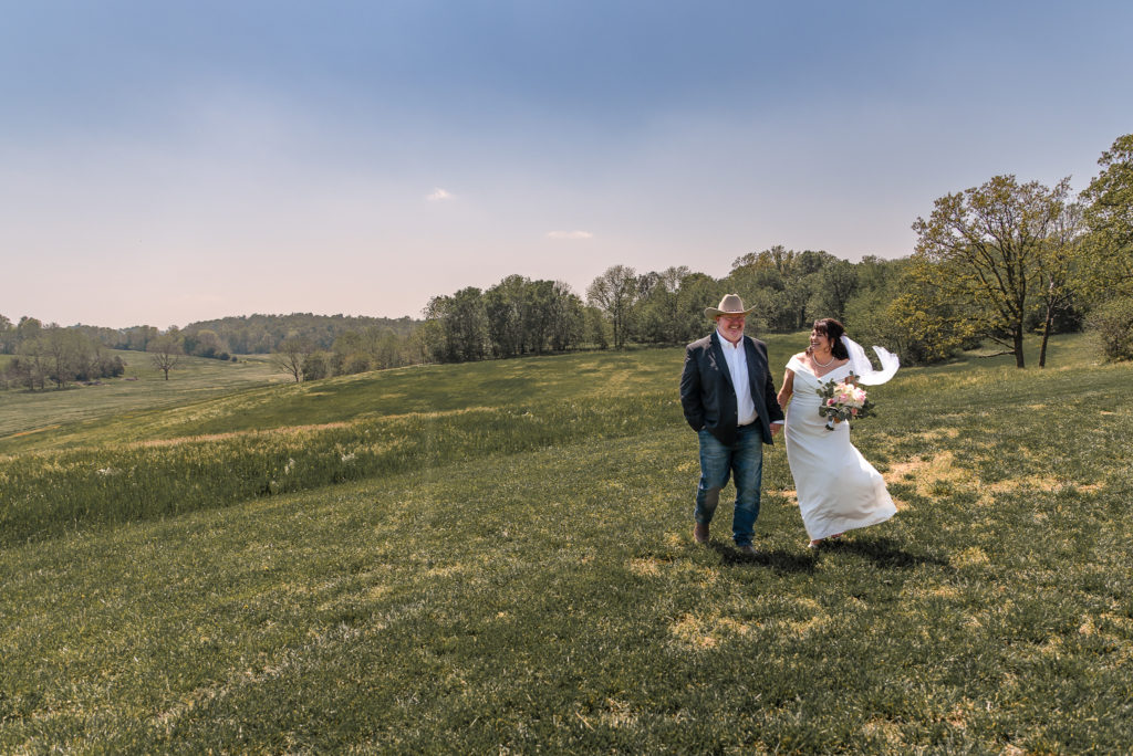 bride and groom walk through field during portrait photos on their wedding day
