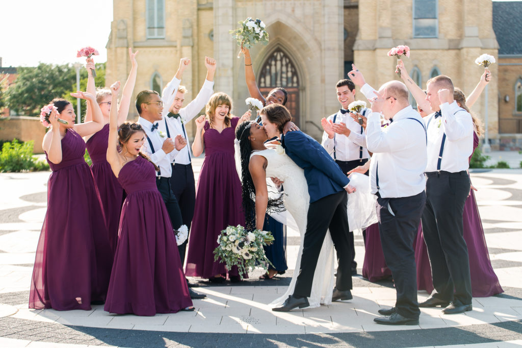 bride and groom kissing while wedding party cheers